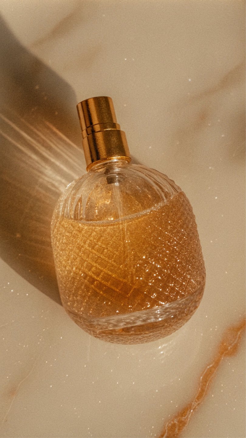 Eine klare Glasparfümflasche mit goldenem Inhalt steht auf Marmor.