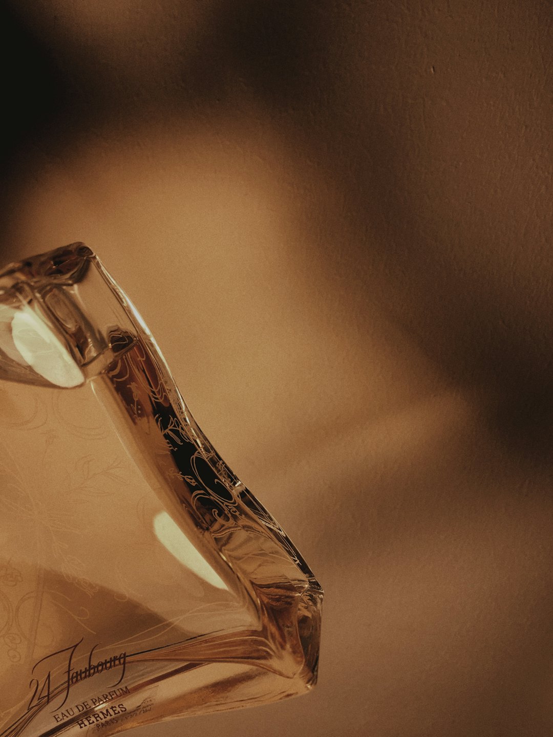 Klarer Glasparfümflakon mit gravierten Details auf beiger Oberfläche.
