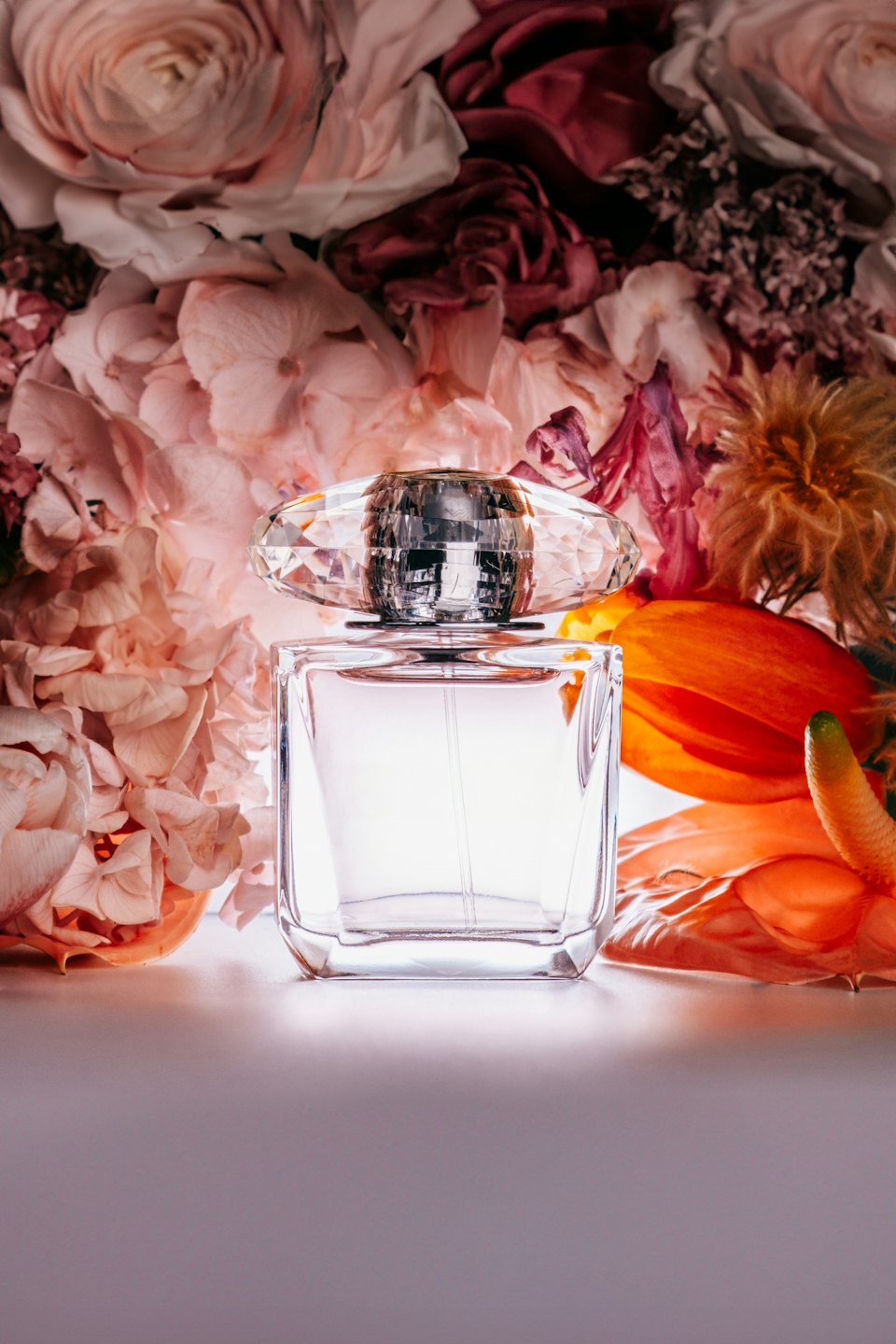 Glasparfümflasche mit Diamantverschluss vor einem Blumenstrauß.